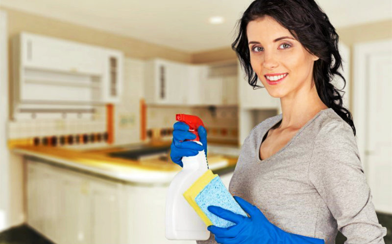 beautiful young woman holding spray bottle and sponge in hand wearing protective gloves