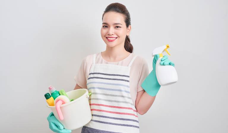Woman in t-shirt and blue gloves holding a white basket and white bottle