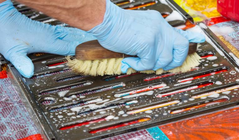 hand of a man in blue gloves scrubbing grill with brush
