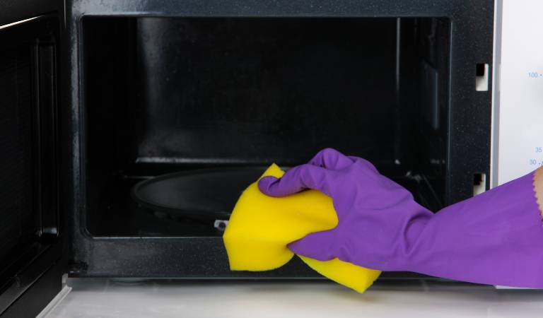 hand in purple gloves scrubbing oven with yellow scrubber