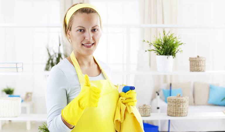 Woman in yellow gloves holding a bottle in her hand inside a room