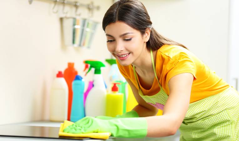 Woman in green gloves and yellow top scrubbing a surface with yellow cloth