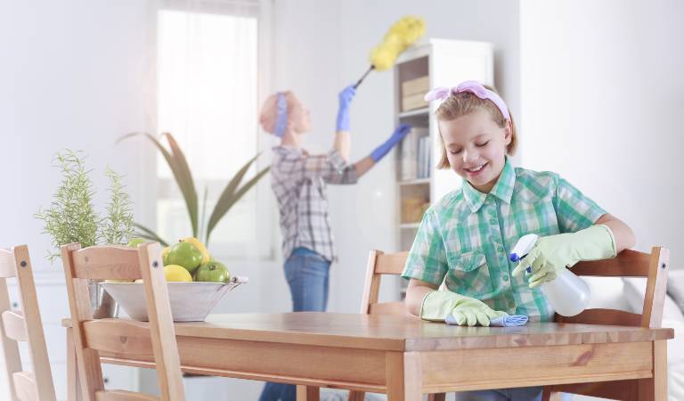 A child is scrubbing a table with white spray bottle