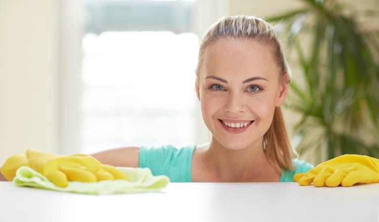 Woman in blue top and yellow gloves smiling and scrubbing a table