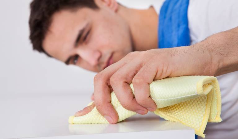 Man holding a cloth scrubbing a table inside a room.