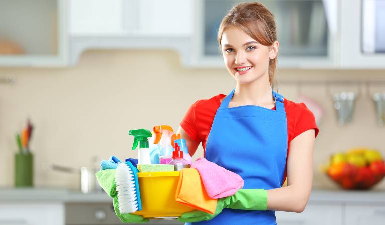 Woman in blue-red top holding a yellow basket filled with bottles, tools and supplies.