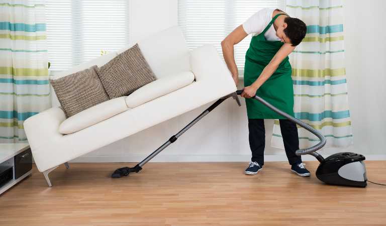 Man in green-white uniform vacuuming wooden floor using stem mop.