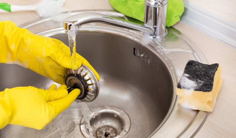 Close up of female hands with rubber gloves cleaning kitchen sink and drain