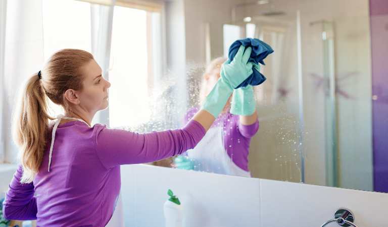 Woman in purple dress cleaning mirror inside a bathroom