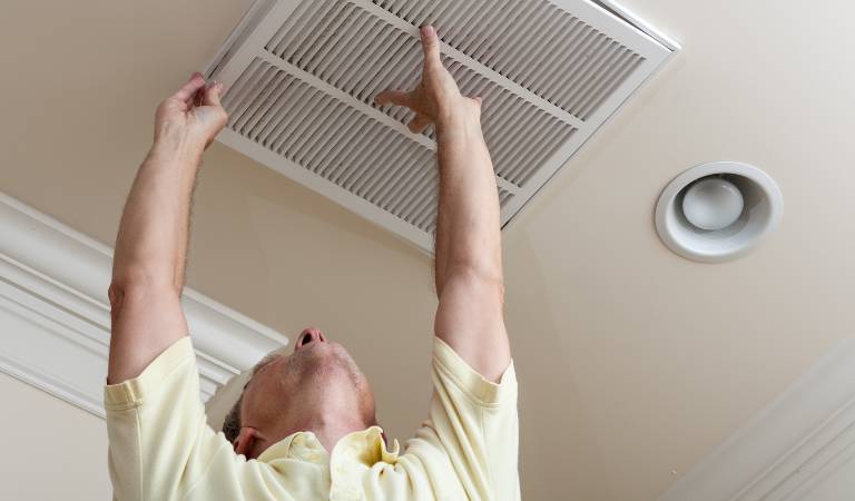 Senior male reaching up to open filter holder for HVAC system.