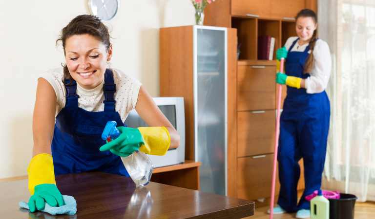 Group of cleaners in uniform performing the task of end of lease cleaning inside a living room.