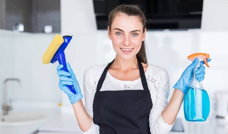 Professional cleaner in white-black uniform holding a brush and bottle in her hand.