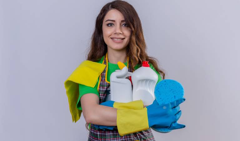 Woman holding cleaning bottles and tools in her arms