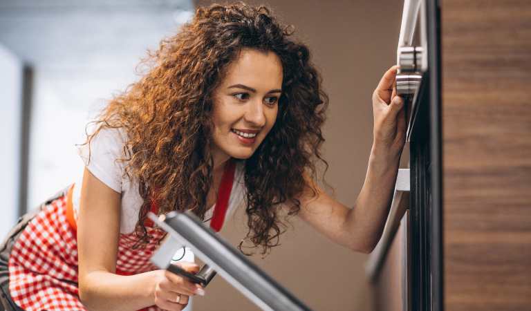 Woman with curly hair holding a swipe and opening her oven glass door.