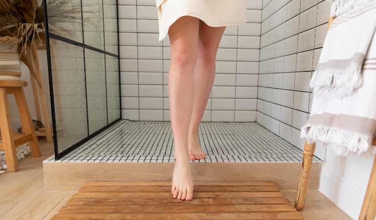 Leg of a woman on pebble shower floor inside her bathroom.
