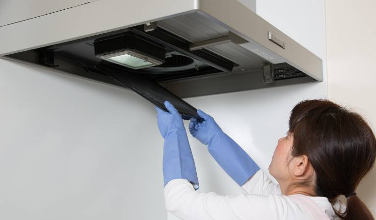 Woman in white dress and blue glove cleaning air ducts.