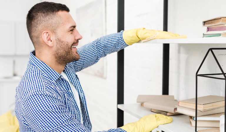 Man in blue shirt and yellow glove cleaning shelves with a cloth
