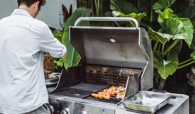 Man in shirt cooking something on BBQ.