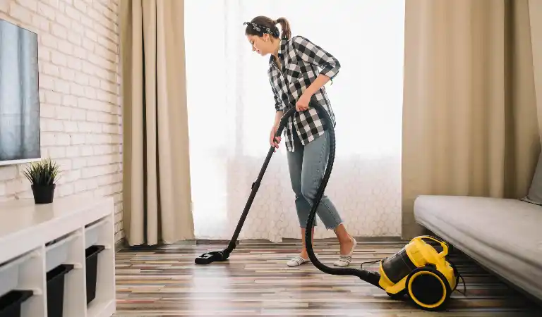 Woman in check shirt and jeans using vacuum cleaner to clean her floor.