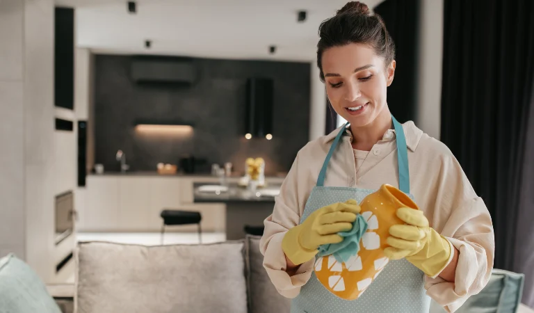 Woman in yellow glove cleaning a vase with a cloth