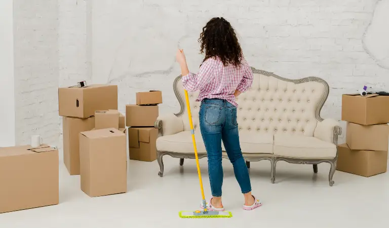 Woman from back holding a cleaning stick in her hand with lots of moving boxes on the floor.