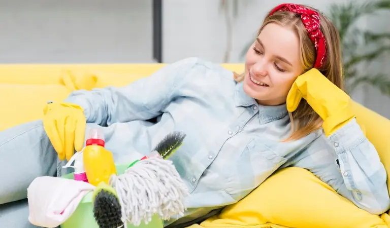 Woman in shirt and yellow gloves on yellow sofa with a cleaning basket.