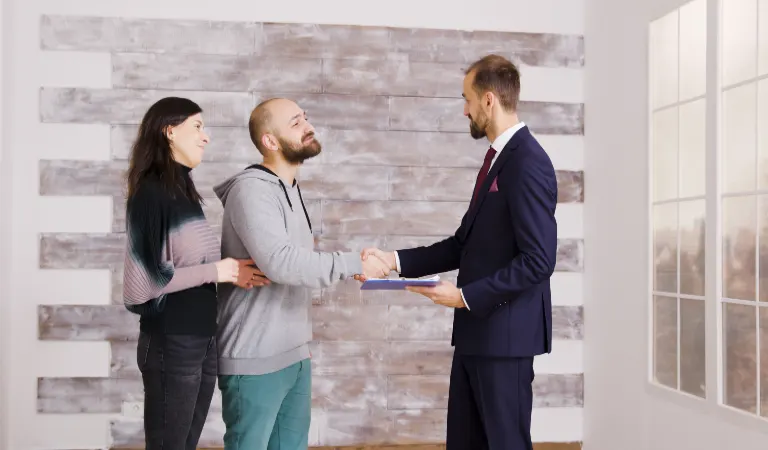 A couple is shaking hand with a landlord in black suit