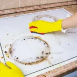 Person cleaning greasy stove with yellow gloves and sponge