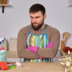 Bearded man in the kitchen, shows all his cleaning staff - detergents, brushes, sprays