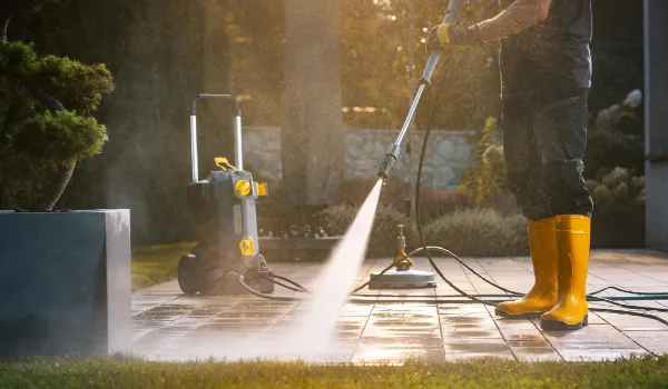 A person power washing a patio with a pressure washer in a sunny outdoor setting