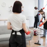 Group of janitors in uniform cleaning office with cleaning equipment