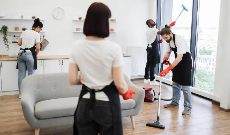 Group of janitors in uniform cleaning office with cleaning equipment