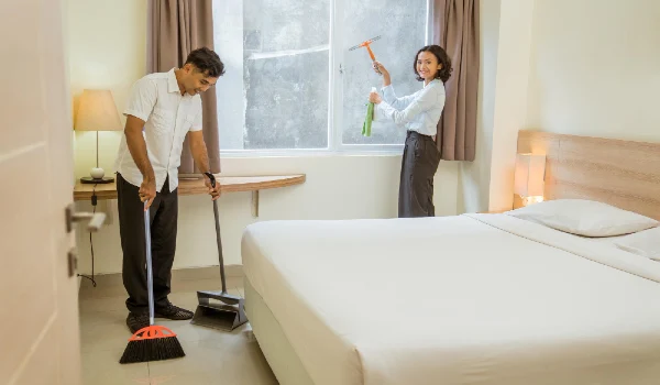 Two cleaning staff working cleaning the room with cleaning equipment in the hotel room