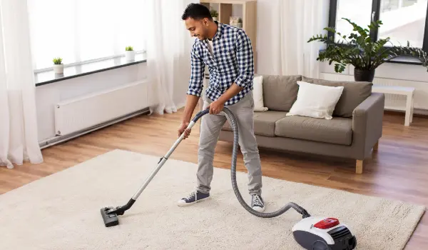 A man with vacuum cleaning floor and rug in living room at home