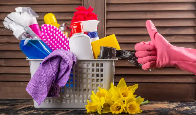 Showing thumbs up and cleaning products in a basket with flowers beside it