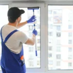 Male professional cleaning service worker in overalls cleans the windows
